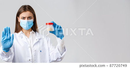 Covid-19, preventing virus, healthcare workers and quarantine concept. Serious concerned doctor in medical mask and PPE, tell to stop using this pills, showing bad medicine or antibiotics 87720749