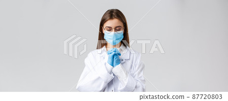 Covid-19, preventing virus, health, healthcare workers and quarantine concept. Hopeful doctor in scrubs and medical mask, personal protective equipment, praying with hands clasped together, hope 87720803