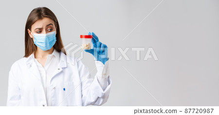 Covid-19, preventing virus, healthcare workers and quarantine concept. Unsure, curious doctor in scrubs and medical mask look intrigued and uncertain at container with medicine pills Covid-19, preventing virus, healthcare workers and quarantine concept. Unsure, curious doctor in scrubs and medical mask look intrigued and uncertain at container with medicine pills 87720987