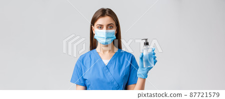 Covid-19, preventing virus, healthcare workers concept. Young pretty professional doctor, female nurse in medical mask and scrubs, showing hand sanitizer or soap to protect from coronavirus Covid-19, preventing virus, healthcare workers concept. Young pretty professional doctor, female nurse in medical mask and scrubs, showing hand sanitizer or soap to protect from coronavirus 87721579