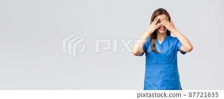 Healthcare workers, prevent virus, insurance and medicine concept. Cute female nurse or doctor in clinic wearing scrubs, cover eyes and peeking through fingers with intrigued smile 87721635
