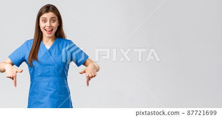 Healthcare workers, prevent virus, covid-19 test screening, medicine concept. Excited happy attractive nurse or doctor in blue scrubs, pointing fingers down, found great promo, showing banner 87721699