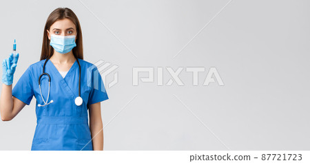 Covid-19, preventing virus, health, healthcare workers and quarantine concept. Serious female nurse in blue scrubs, doctor wearing medical mask holding syringe with coronavirus vaccine 87721723