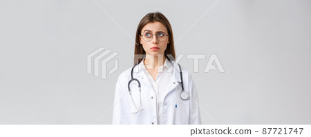 Healthcare workers, medicine, insurance and covid-19 pandemic concept. Doctor see something strange. Confused and suspicious female doctor in white scrubs, glasses, frowning and staring left 87721747