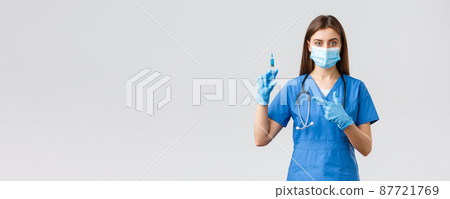 Covid-19, preventing virus, health, healthcare workers and quarantine concept. Serious female nurse or doctor in blue scrubs, medical mask, pointing at syringe with coronavirus vaccine 87721769