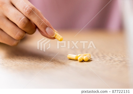 A woman's hand picking a capsule tablet on the table with her fingers A woman's hand picking a capsule tablet on the table with her fingers 87722131