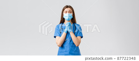 Covid-19, preventing virus, health, healthcare workers and quarantine concept. Hopeful female nurse or doctor in blue scrubs, medical mask, praying for lives of patients sick coronavirus infection 87722348