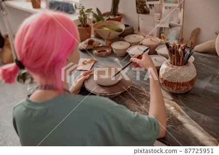 Female ceramist decorating earthenware in ceramic workshop 87725951