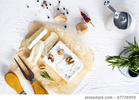 Cheese, herbs, nuts and knife on white table. Overhead view. Selective fucus. 87726959