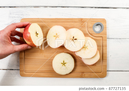 Fresh apple cut into slices on a bamboo cutting board. Woman hand 87727135