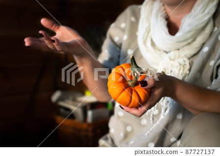 A woman with a small orange pumpkin in her hands. Front view. 87727137