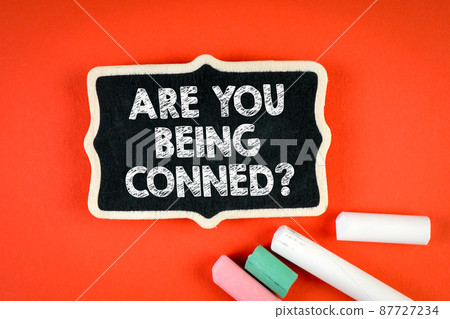 Are You Being Conned. Miniature chalk board with chalk pieces on red background 87727234