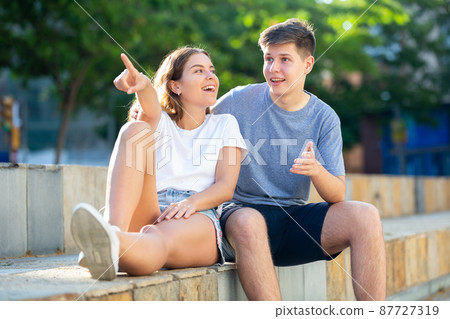 Girl prompts the boy, pointing with his hand at something 87727319