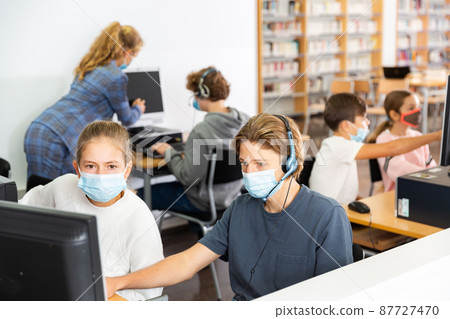 Teenagers wearing masks in computer class in library Teenagers wearing masks in computer class in library 87727470