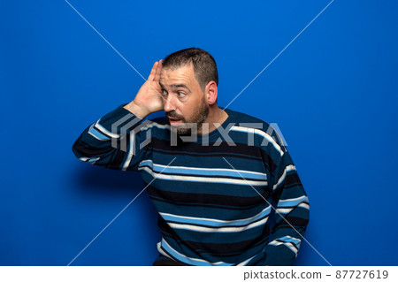 Handsome middle age man with brunette hair over isolated blue background with hand on ear listening to rumor or gossip. Deafness concept. Handsome middle age man with brunette hair over isolated blue background with hand on ear listening to rumor or gossip. Deafness concept. 87727619