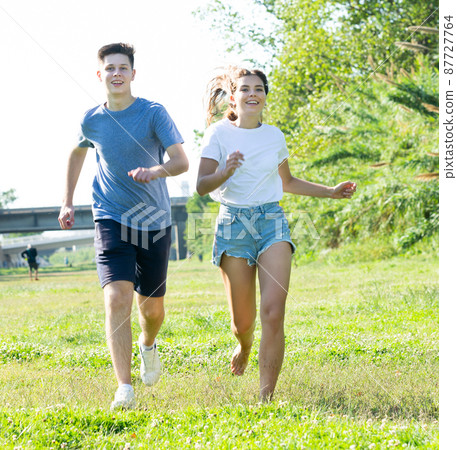 Laughing teenagers playing outdoors funning at grass on day Laughing teenagers playing outdoors funning at grass on day 87727764