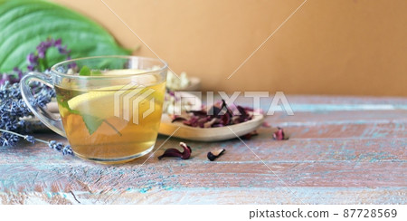 Cup of green tea with mint and lemon, dry petals of useful plants on a wooden table 87728569