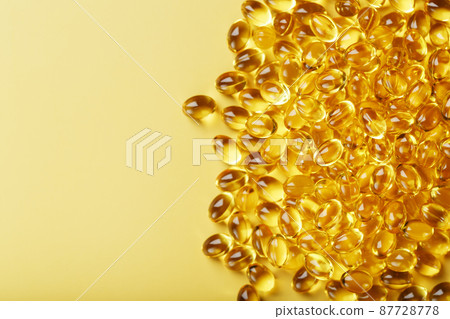 Pile of golden capsules of vitamin D3 on a yellow background with free space 87728778