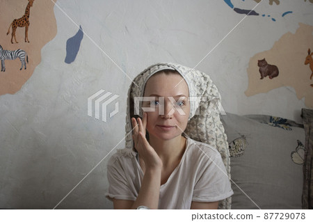 An attractive happy woman of thirty years smears her cheeks with cream, a towel on her head, a home beauty ritual every day 87729078