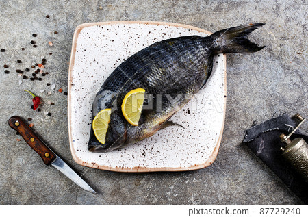 Fresh fish dorado. Dorado and ingredients for cooking at black slate table. Top view with copy space. Fresh fish dorado. Dorado and ingredients for cooking at black slate table. Top view with copy space. 87729240