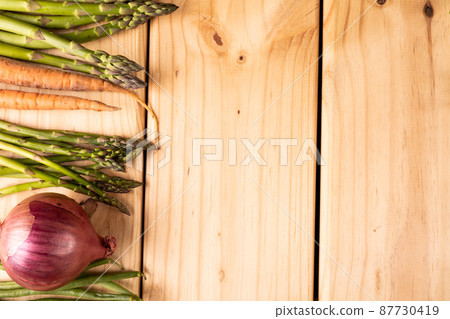 Overhead view of asparagus with carrots and onion on wooden table with blank space 87730419