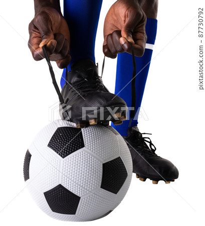 Low section of african american male soccer player tying shoelace on ball against white background Low section of african american male soccer player tying shoelace on ball against white background 87730792