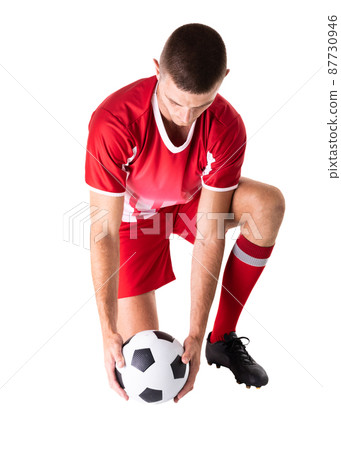 Full length of caucasian young male soccer player kneeling while holding ball over white background 87730946