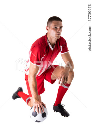 Full length of caucasian young male athlete kneeling by soccer ball against white background 87730978