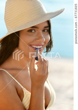 smiling woman in bikini with lip balm on beach 87731605
