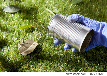 close up of hand in glove with used can on grass 87731688