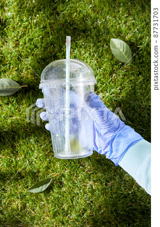 hand in glove removing plastic cup from grass 87731703
