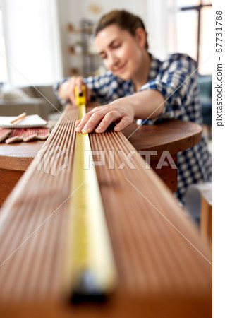 woman with ruler measuring wooden board at home 87731788