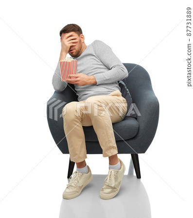 scared man with popcorn sitting in chair 87731889