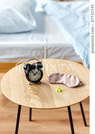 alarm clock, earplugs and sleeping mask on table 87732345