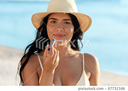 smiling woman in bikini with lip balm on beach 87732386