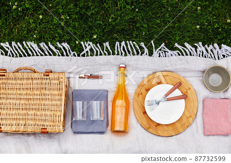 basket, crockery and juice on picnic blanket 87732599