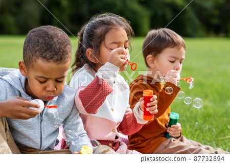 group of children blowing soap bubbles at park 87732894