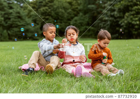 group of children blowing soap bubbles at park 87732910