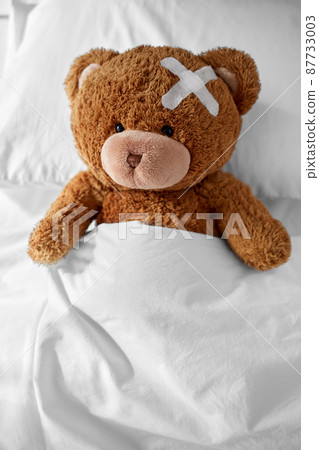 teddy bear with medical patch on head lying in bed teddy bear with medical patch on head lying in bed 87733003