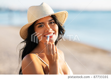smiling woman in bikini with lip balm on beach 87733101