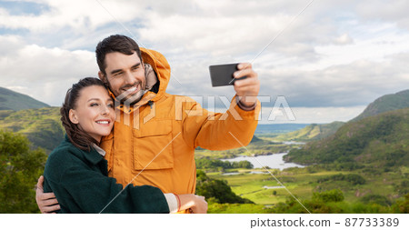 couple taking selfie on phone over irish landscape 87733389