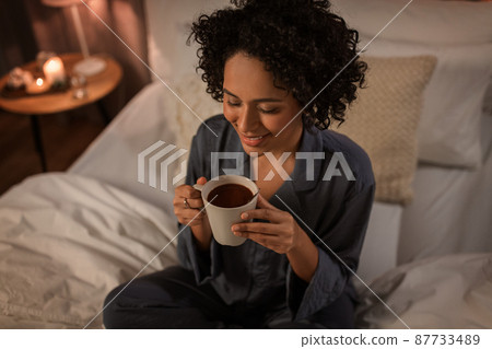 happy woman with hot chocolate sitting in bed happy woman with hot chocolate sitting in bed 87733489