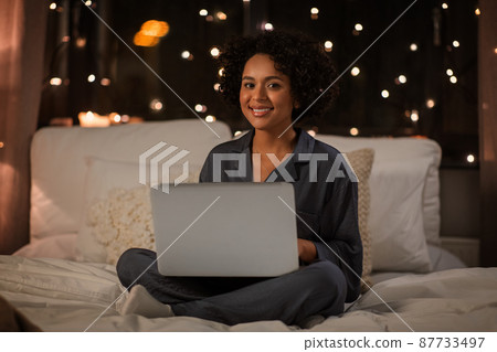 happy woman with laptop sitting in bed at night 87733497