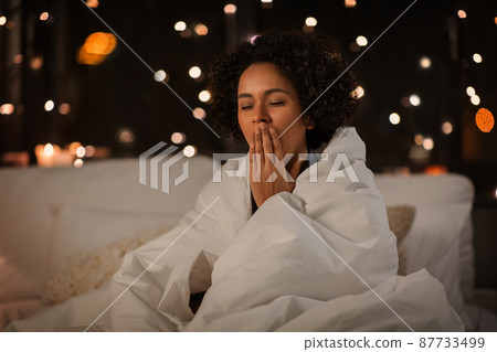 yawning woman wrapped in blanket in bed at night 87733499
