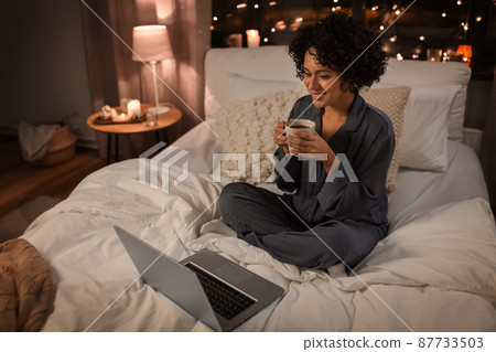 woman with laptop and mug sitting in bed at night woman with laptop and mug sitting in bed at night 87733503