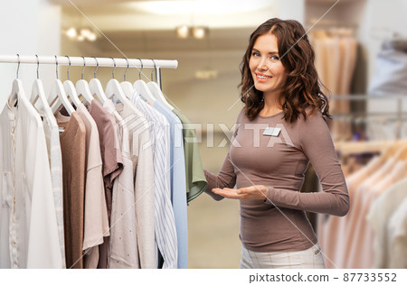 happy female shop assistant with clothes on hanger happy female shop assistant with clothes on hanger 87733552