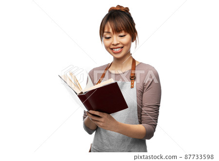 smiling woman in apron reading cook book 87733598