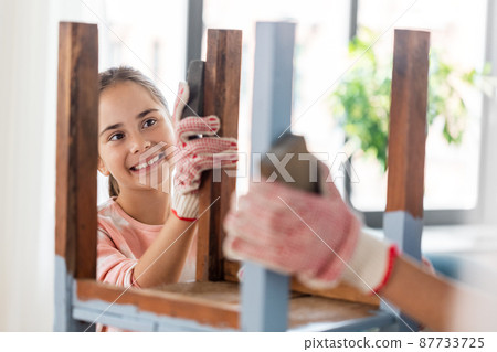 smiling girl sanding old table with sponge at home 87733725