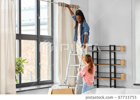 woman on ladder hanging curtains at home 87733755