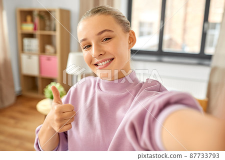 girl taking selfie and showing thumbs up at home 87733793
